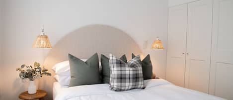 A neatly made bed with a headboard, a bedside table with a lamp, and a wardrobe.