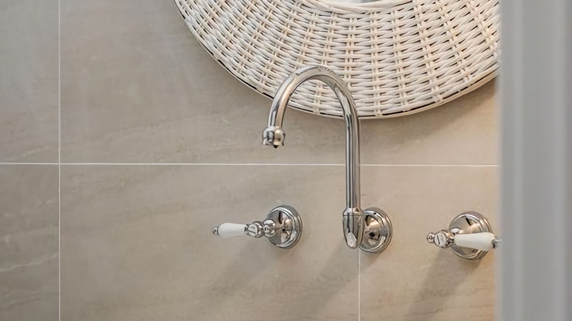 A bathroom with a wall-mounted shower head, a white wicker bath mat, and a tiled floor.