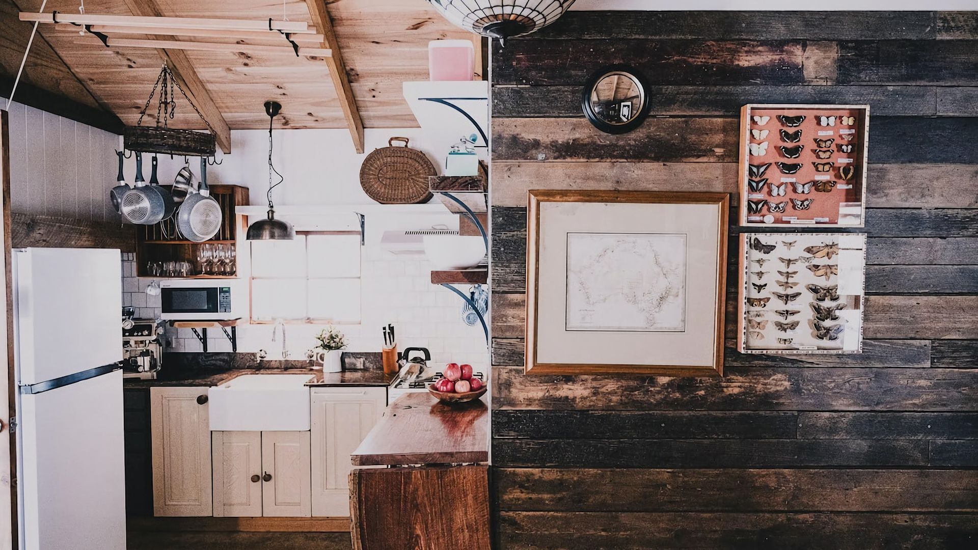 A rustic kitchen with wooden beams, a hanging light fixture, and a variety of kitchen utensils.