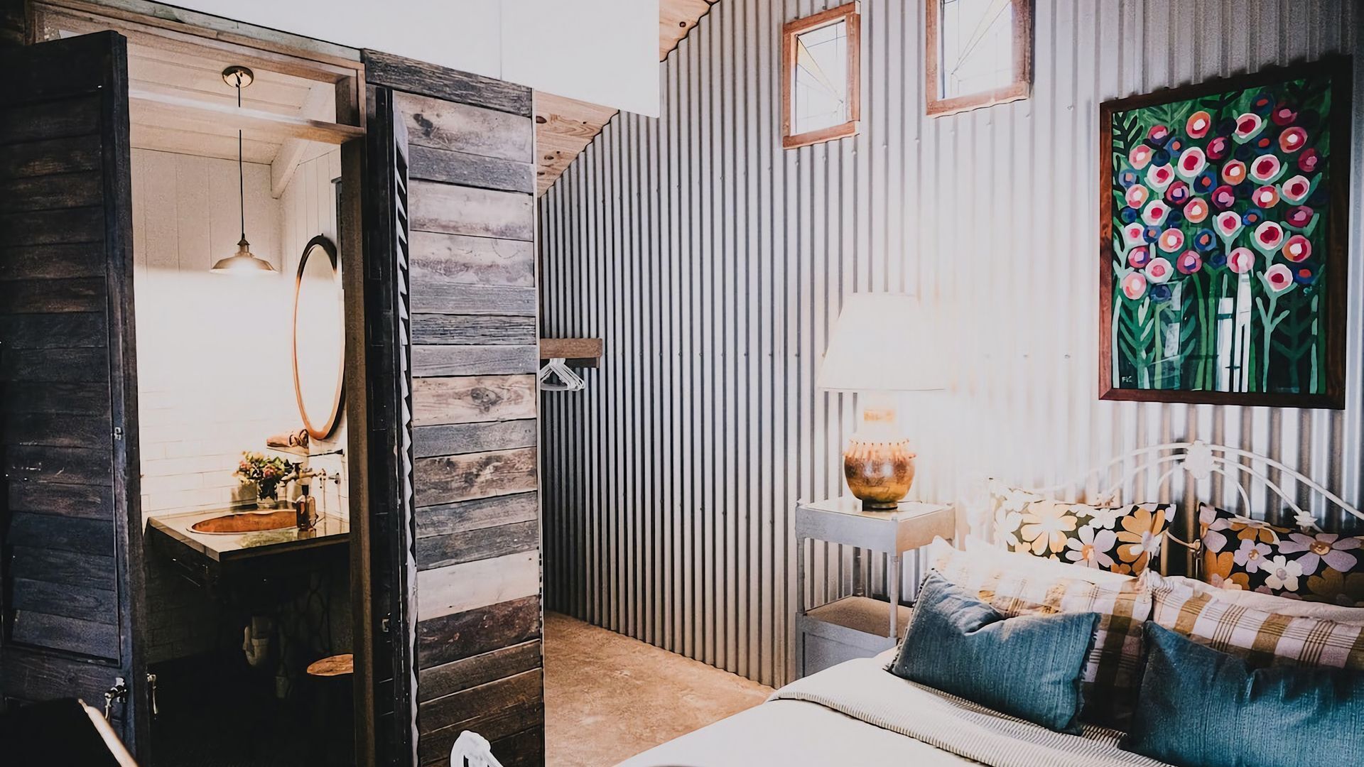 A bedroom with a bed, bedside table, lamp, and a floral painting on the wall.