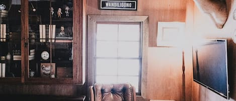 A room with a leather armchair, a small table, a mounted deer head, and a bookshelf with figurines.