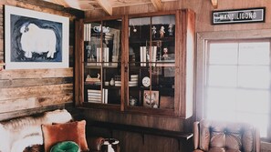 A room with a wooden cabinet containing books, a framed picture of a pig, and a sign reading 'WANDILIGONG'. - La Baracca - Reconnect with the simple pleasures of life (Wandiligong)