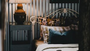 Una cama con almohadillas de estampado floral y un cabecero, una mesita de noche con una lámpara, y una pared con rayas verticales.