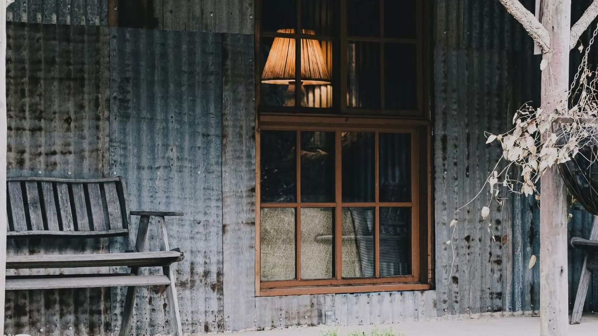 Une cabane rustique avec une fenêtre en bois, un banc et une plante suspendue.
