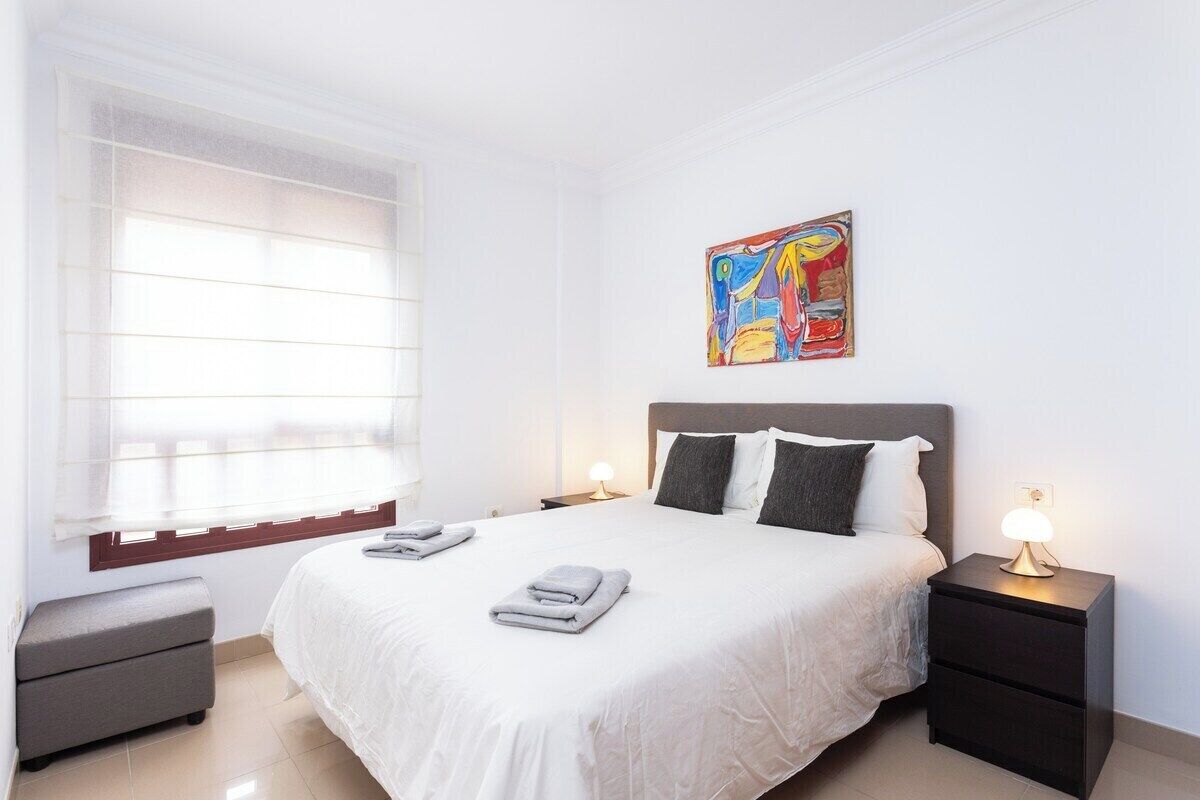 A neatly arranged hotel room with a large bed, a bedside table with a lamp, and a window with blinds.