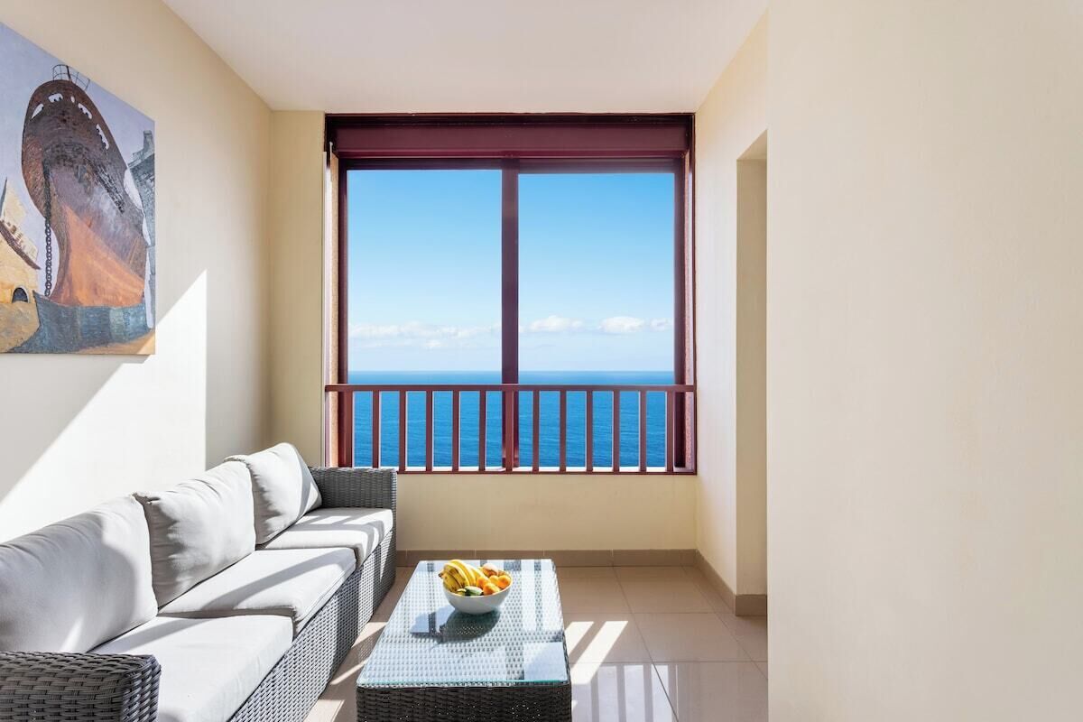 A balcony with a sofa and a table, overlooking a clear blue sea.