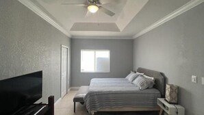 A bedroom with a bed, a ceiling fan, a TV, and a window. - Homestead Green retreat (Homestead)