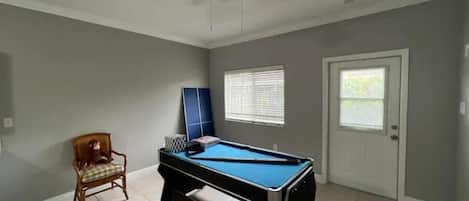 Una habitación con mesa de billar, ventilador de techo, una puerta y una ventana.