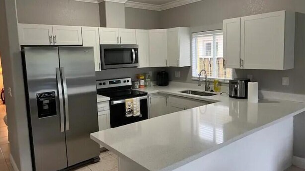 A modern kitchen with white cabinets, stainless steel appliances, and a large island. - Homestead Green retreat (Homestead)