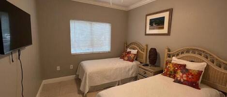 A bedroom with two beds, a ceiling fan, a television, and a window with blinds.