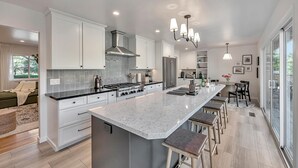 A modern kitchen with white cabinetry, a large island, stainless steel appliances, and pendant lighting.