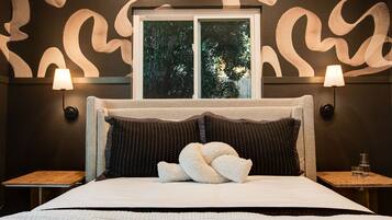 Een hotelkamer met een groot bed, twee bedlampjes, een raam met uitzicht op bomen en een kamer met een patroon op de muur.