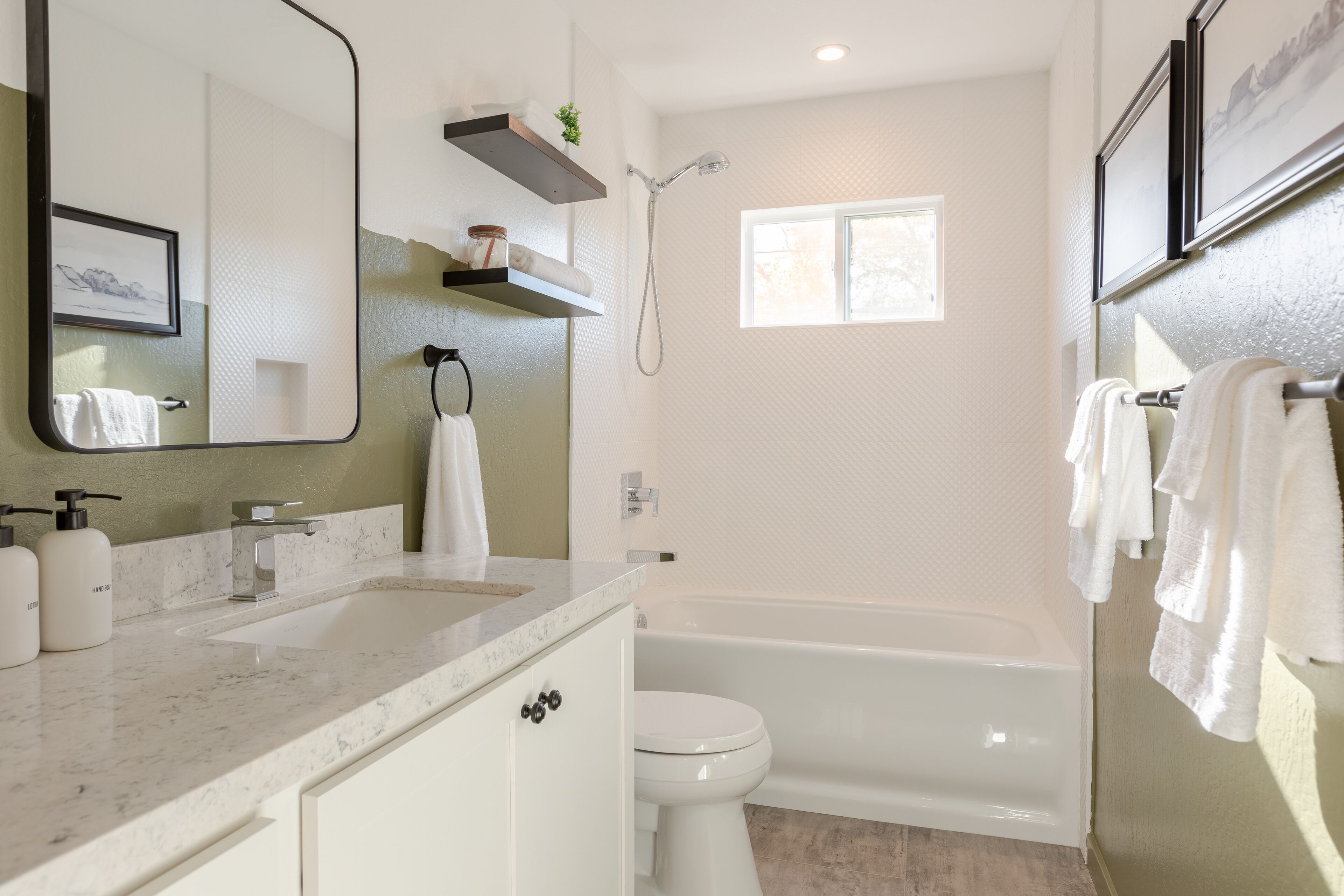 A modern bathroom with a large mirror, a bathtub, a toilet, and a sink.