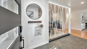 A modern interior with a glass door, a round mirror, a hanging bag, and a rope swing.