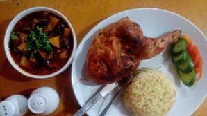 Une assiette contenant un morceau de poulet rôti, du riz et des légumes coupés en tranches.