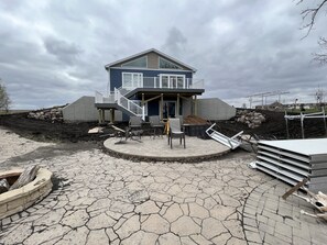 A two-story house with a balcony, a patio with chairs, and a stone pathway. - Country lake house getaway accommodating large family-sized fun! (Emmetsburg)