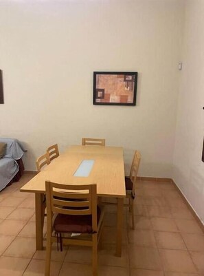 Cozy dining area with a wooden table and chairs, a framed artwork, and a comfortable bed nearby.