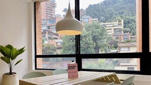 A room with a large window, a wooden table, and a potted plant. - PortaCol By Wynwood House (Bogotá)