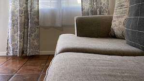 A room with a sofa, patterned curtains, and a view through a window.