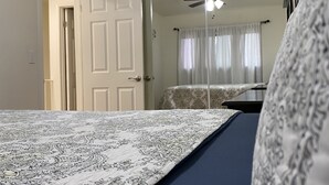 A bedroom with a bed, a ceiling fan, a door, and a mirror.