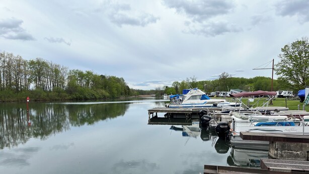 A calm river with boats docked at a pier, surrounded by trees and a cloudy sky. - Explore the Finger Lakes Region from this cozy 3-bedroom home near Geneva, NY. (Waterloo)