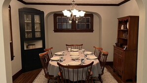 A dining room with a round table set for six, surrounded by wooden chairs. There is a chandelier above the table and a window with a dark frame. - Explore the Finger Lakes Region from this cozy 3-bedroom home near Geneva, NY. (Waterloo)