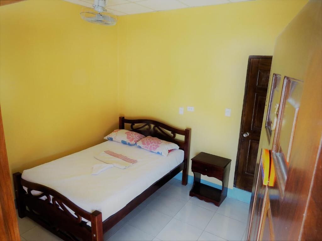 A single bed with a wooden frame, a small bedside table, and a ceiling fan in a room with yellow walls.