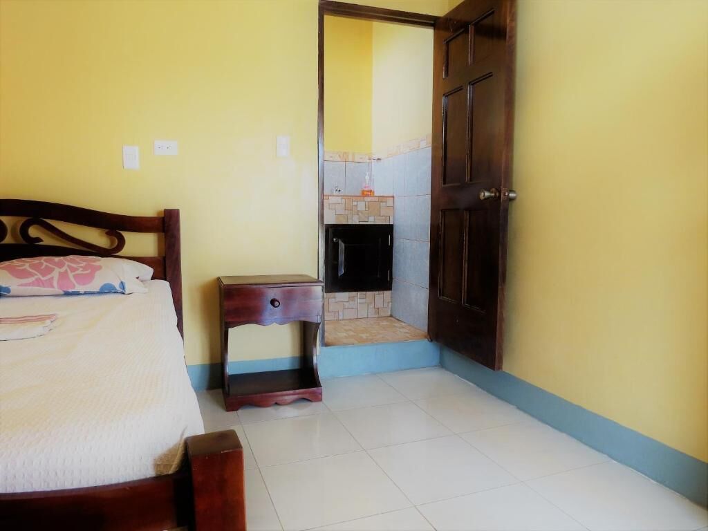 Um quarto com uma cama, uma mesa de cabeceira, uma pequena mesa e uma porta que dá para um banheiro.