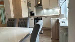 A modern kitchen with a dining area, featuring a white table, grey upholstered chairs, and a built-in oven. - Oase mit Parkplatz, Kaffeeautomat, Balkon und Küche (Untermeitingen)