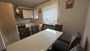 A compact kitchen with a dining table, chairs, and a window with blinds. - Oase mit Parkplatz, Kaffeeautomat, Balkon und Küche (Untermeitingen)