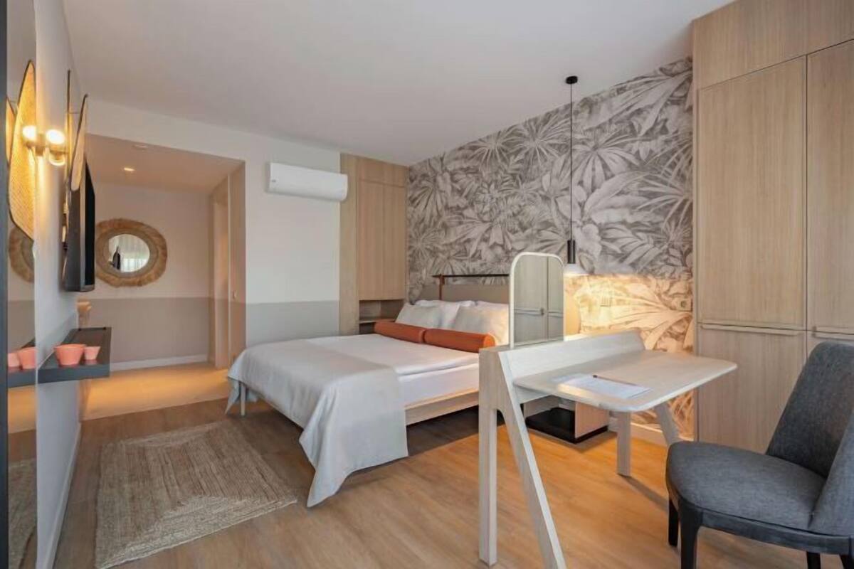 A modern bedroom with a bed, desk, chair, and a mirror.
