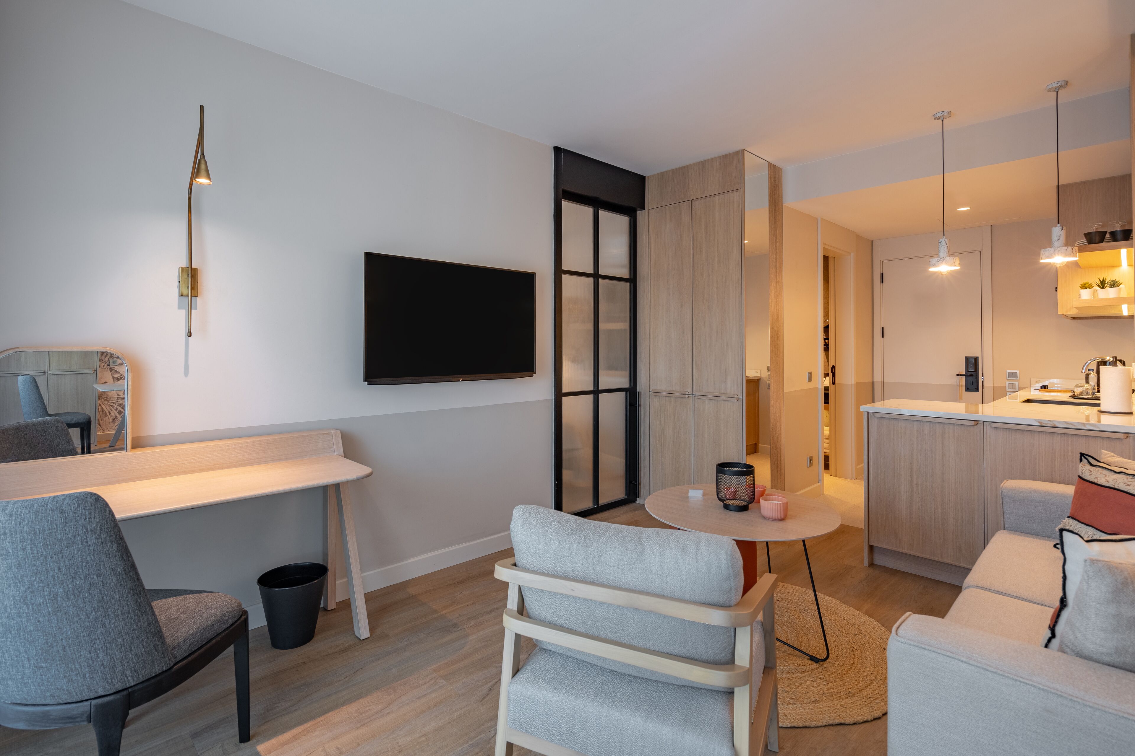 A modern living room with a sofa, a dining table, and a TV mounted on the wall.