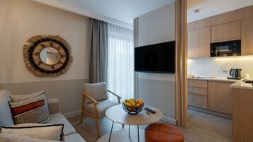 Een moderne woonkamer met een bank, fauteuil, ronde tafel met fruit, en een televisie.