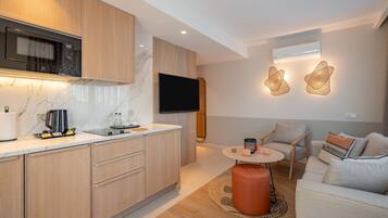 A modern kitchen with a microwave, stove, and sink. There is a flat-screen TV mounted on the wall, a small round table with chairs, and a sofa with cushions.