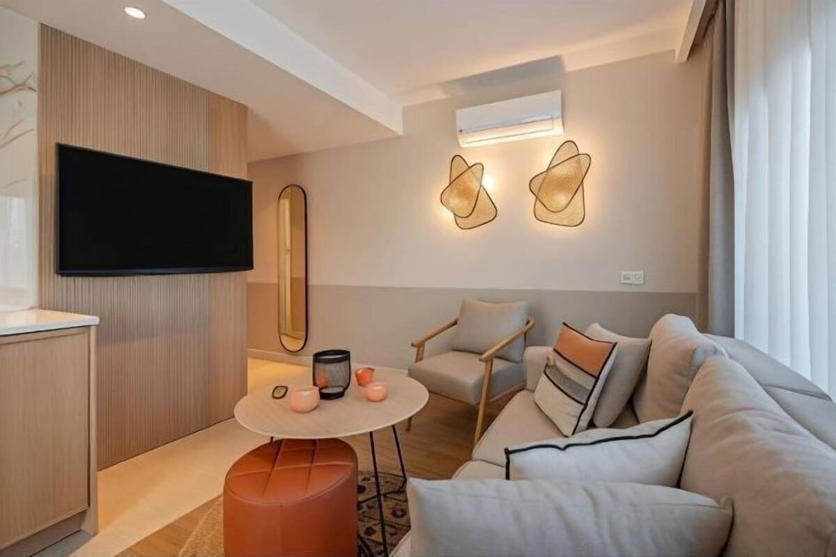 A modern living room with a flat-screen TV, a round table with candles, a sofa with cushions, and abstract wall art.