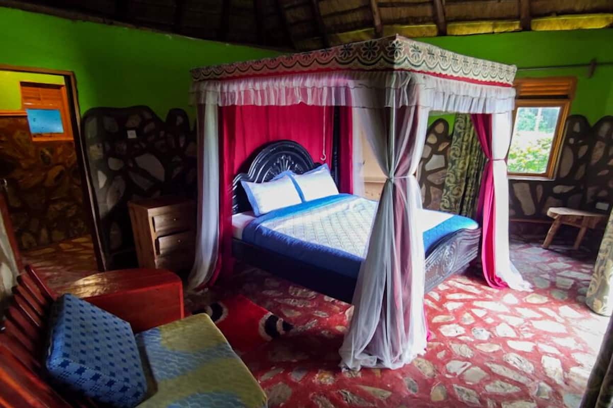 A room with a bed under a canopy, a red and white patterned carpet, and a stone wall.