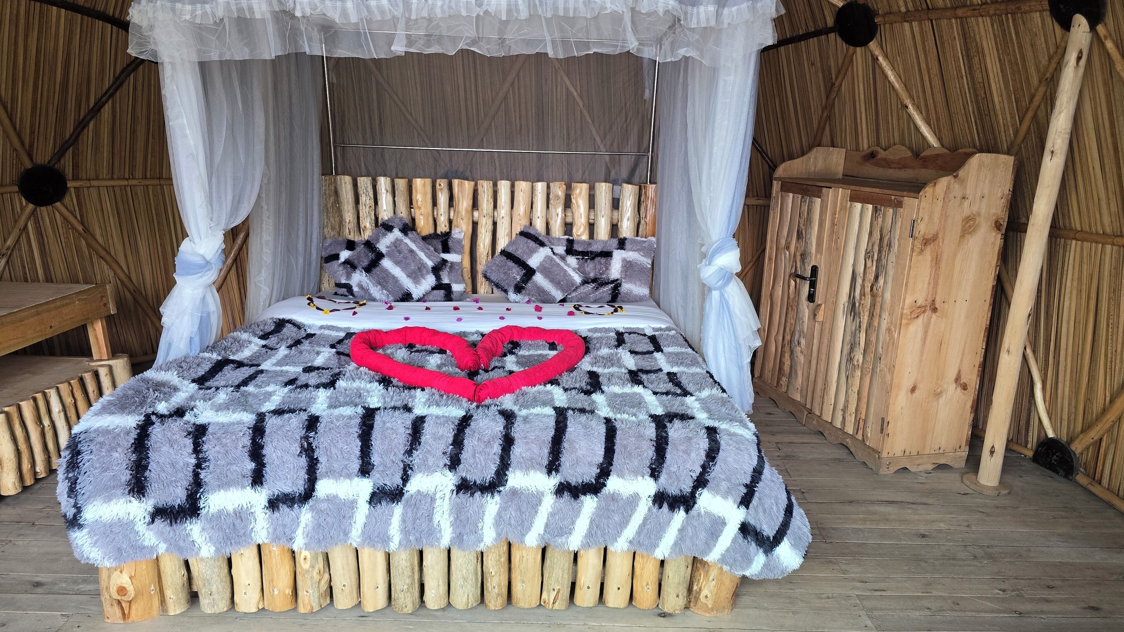 Una cama de madera rústica con dosel, un cojín con forma de corazón y una colcha a cuadros.