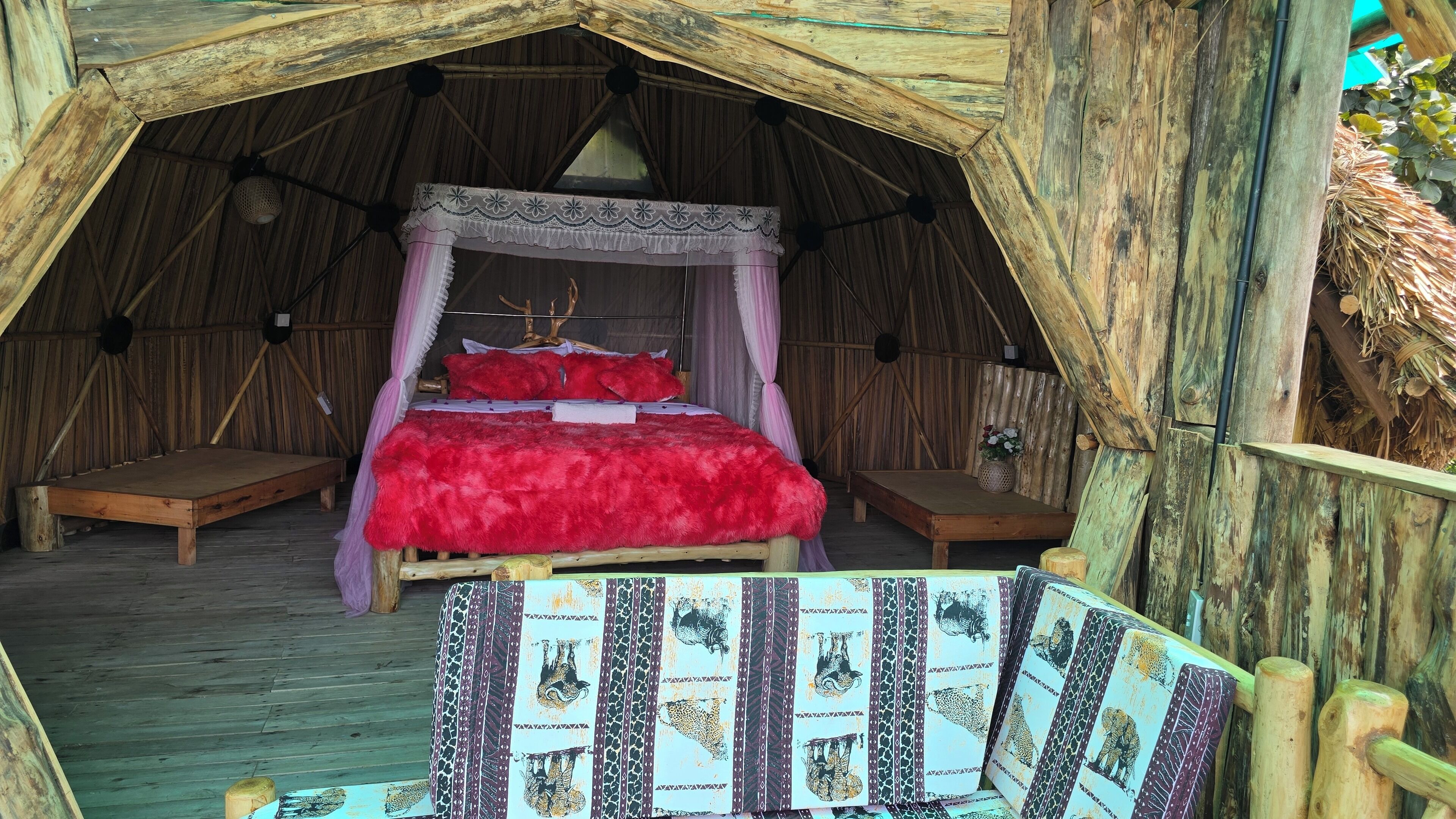 Una habitación tipo tienda de campaña acogedora y rústica, con una cama grande, un banco de madera y una cortina decorativa.