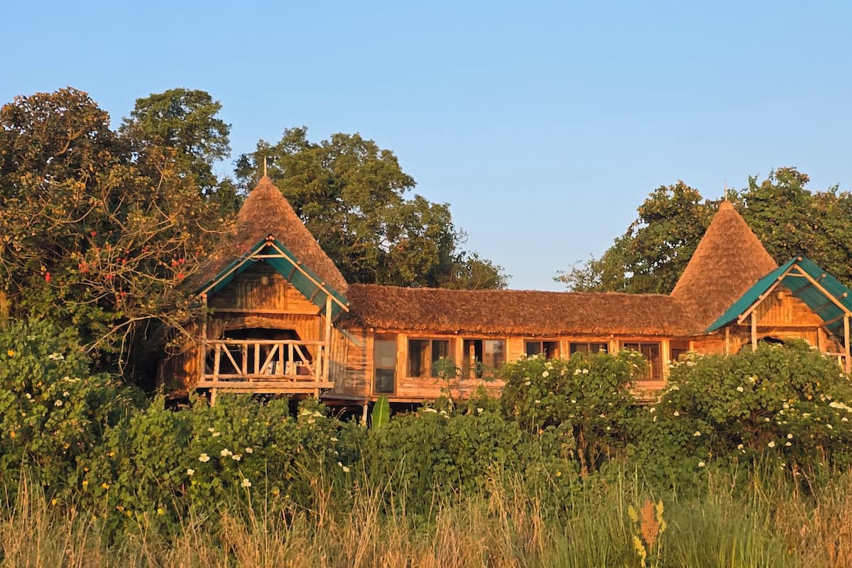 A rustic wooden building with a thatched roof, surrounded by lush greenery and flowering plants.
