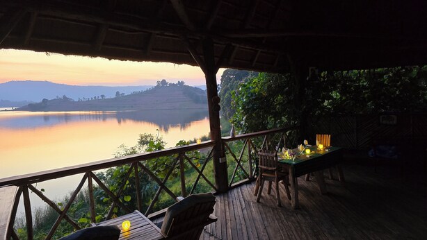 Una terraza de madera con mesa y sillas que da a un lago tranquilo al atardecer.