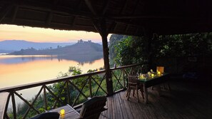 A wooden deck with a table and chairs overlooking a calm lake at sunset. - Paradise Eco Hub  (Itambira Island)