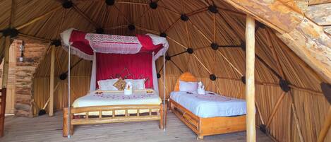 A cozy, rustic tent-style bedroom with two wooden beds, a canopy bed, and a stone wall backdrop.