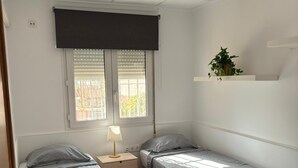 Une petite chambre propre, avec deux lits, une table de chevet, une lampe et une fenêtre avec des stores.