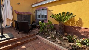 Une terrasse avec des meubles d’extérieur, un petit jardin et un mur jaune.