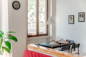 A dining area with a table set for two, a clock on the wall, and a window with a view of buildings. - Terrazza Rooftop - My Home in Como (Como)