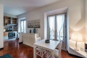 A compact kitchen with modern appliances, a dining area with a white table, and a balcony with curtains.