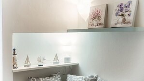 A room with a white wall, a shelf with decorative items, and a bed with patterned pillows. - Celeste - My Home In Como (Como)