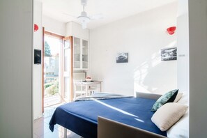 Une chambre à coucher comprenant un lit, un bureau et une chaise, un ventilateur de plafond et une vue sur l’extérieur.