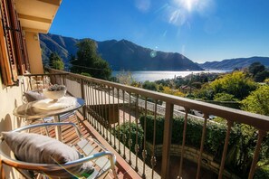 A balcony with a view of a lake and mountains, a table with chairs, and a railing.
