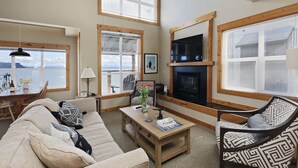A cozy living room with a fireplace, large windows, a dining area, and a view of the water.